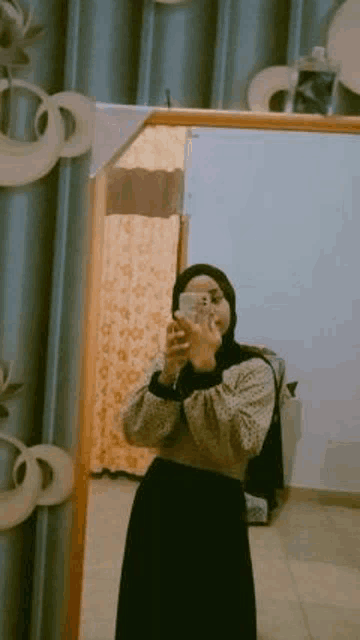 a woman is taking a selfie in front of a mirror while wearing a hijab .