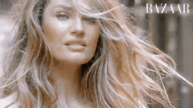 a woman with long blonde hair is standing in front of a building with her hair blowing in the wind .