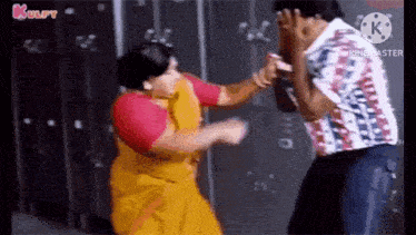 a man and a woman are fighting in front of lockers . the woman is wearing a yellow saree .