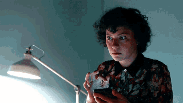 a woman in a floral shirt is looking at her cell phone