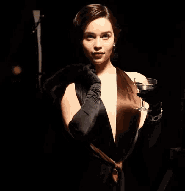 a woman in a black dress and long black gloves holds a glass of wine