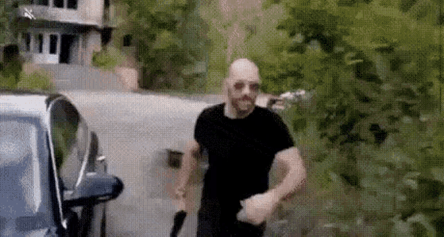 a man in a black shirt is holding a knife while walking towards a car .