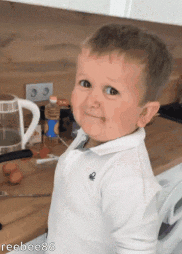 a little boy wearing a white shirt with a blue circle on the sleeve looks at the camera