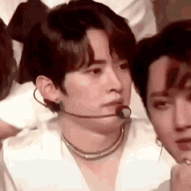 a young man wearing a microphone and a necklace is sitting next to another young man .