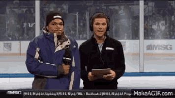 two men are standing on a hockey rink talking into microphones .