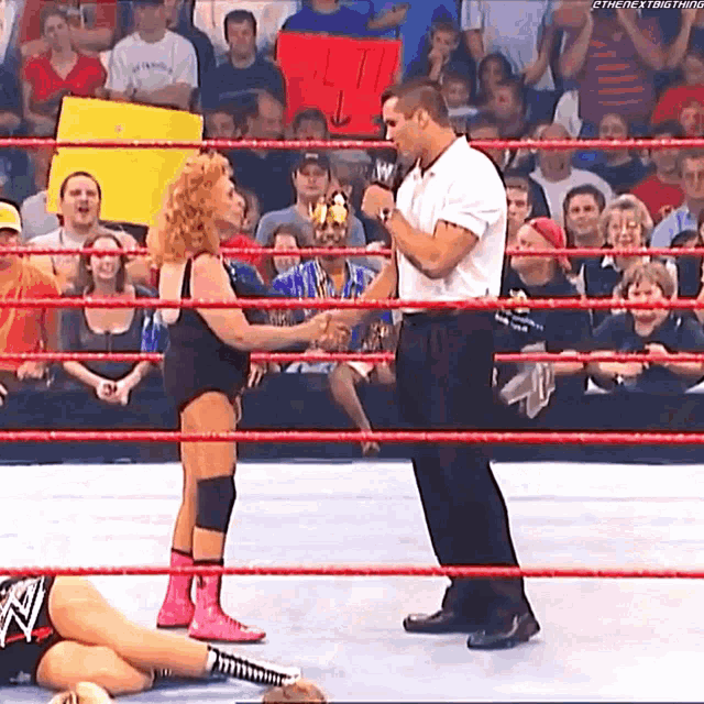 a man in a white shirt stands in a wrestling ring talking to a woman