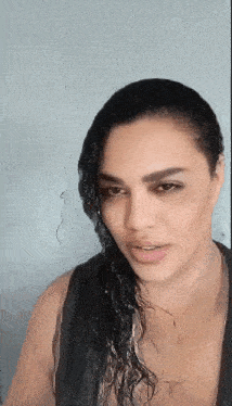 a woman with wet hair is wearing a black tank top and looking at the camera .