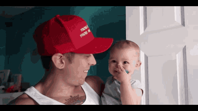 a man holding a baby wearing a red hat that says you 're 1 you 're on