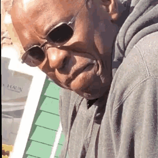 a man wearing sunglasses and a grey hoodie is looking down