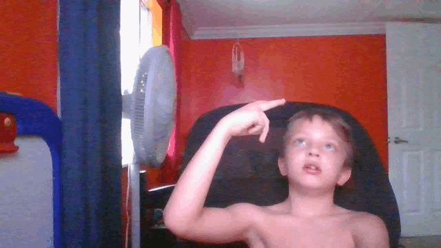 a young boy without a shirt is sitting in front of an orange wall