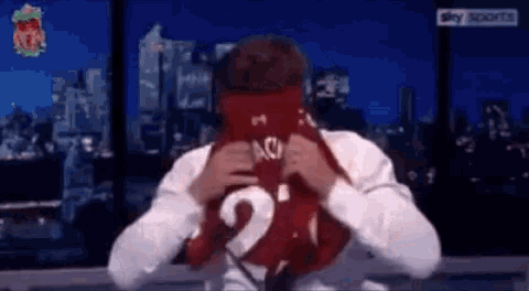 a man in a white shirt is holding a red shirt with the number 21 on it .