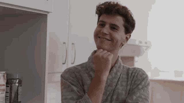 a man in a robe is smiling in a kitchen .