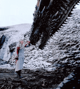 a woman standing next to a large dragon in the snow .