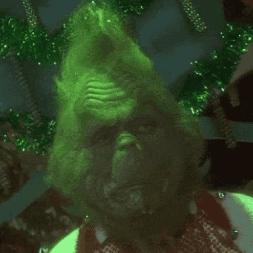a close up of a person 's face with green hair and a christmas tree in the background