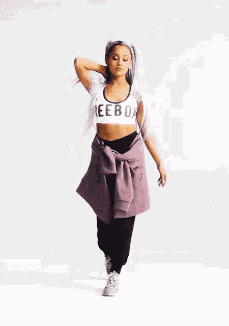 ariana grande is wearing a white sports bra and purple pants .