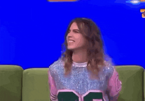 a woman is sitting on a green couch smiling in front of a blue screen .