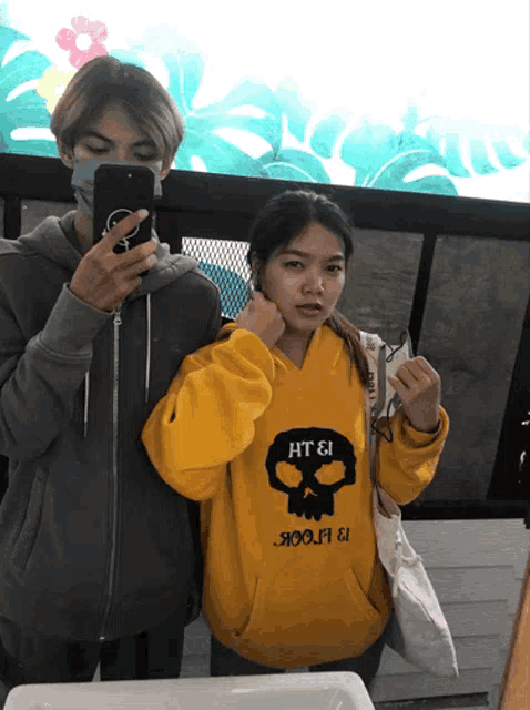 a man taking a picture of a girl in a yellow hoodie that says ht & i