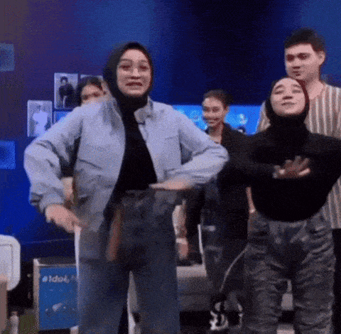 a woman in a hijab is dancing with a group of people in a room .