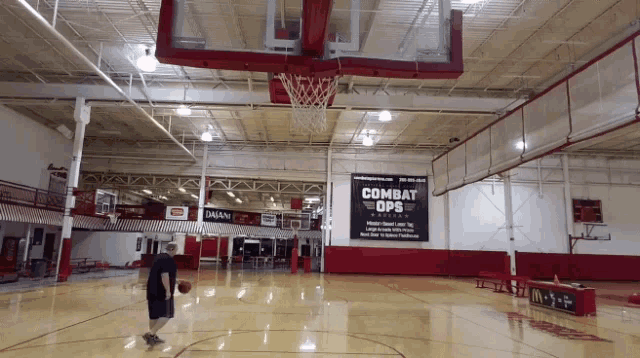 a man dribbles a basketball in a gym with a combat ops sign