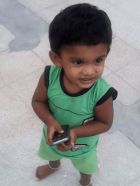 a young boy in a green shirt holds a cell phone in his hand
