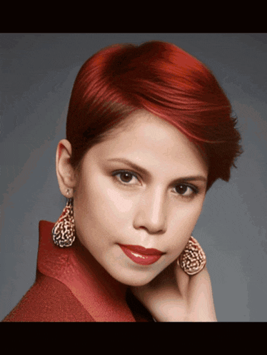 a woman with short red hair wearing earrings and a red jacket