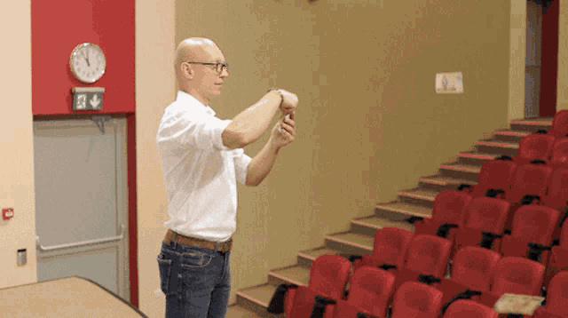 a man in a white shirt stands in front of a red wall with a clock on it