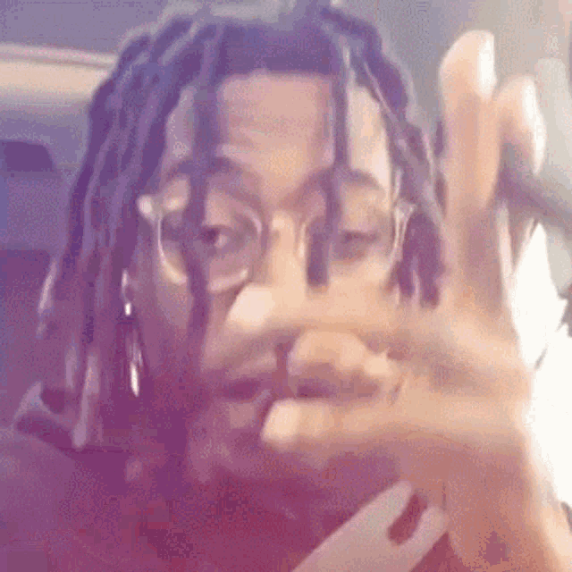 a man with dreadlocks and glasses is making a peace sign .