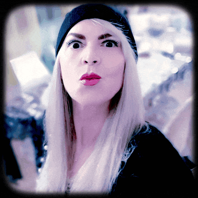 a woman with long blonde hair wearing a black hat looks at the camera