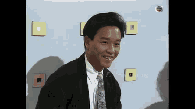 a man in a suit and tie is smiling while sitting in front of a wall with squares on it .