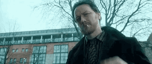 a man with a beard is smoking a cigarette in a park in front of a building .