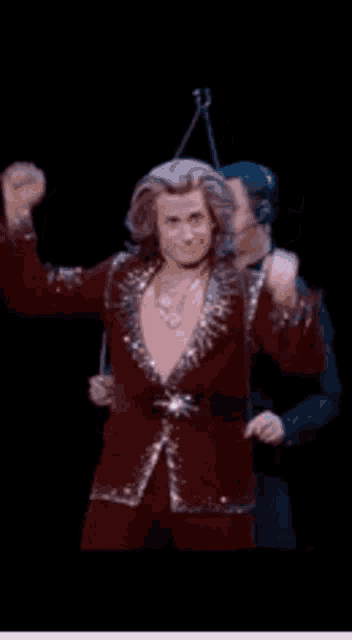 a man in a red suit is dancing on a stage with his fist in the air