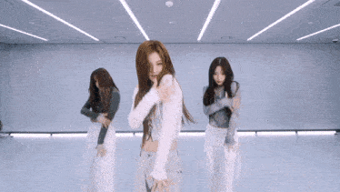 three young women are dancing in a room with a white wall