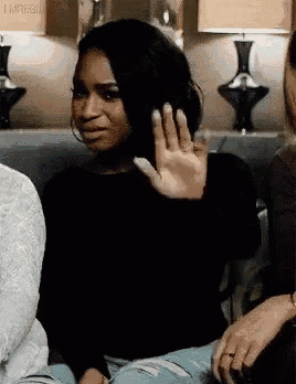 a woman is sitting on a couch with her hand up and making a funny face .