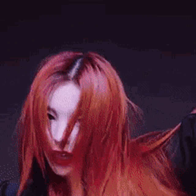 a woman with red hair and black nails is standing in front of an orange wall .