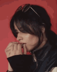 a woman wearing sunglasses and a black jacket is biting her finger