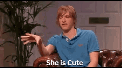 a man in a blue shirt is sitting on a couch and saying she is cute