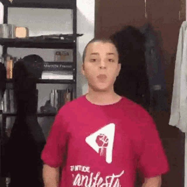 a young man wearing a red t-shirt is standing in front of a shelf .