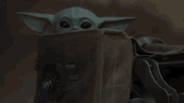 a baby yoda is sitting in a brown bag and looking out