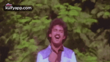 a man is standing in front of a forest with his arms outstretched and smiling .