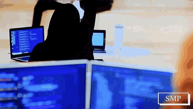 a person sitting at a desk with a laptop and two monitors with the word smp on the bottom right