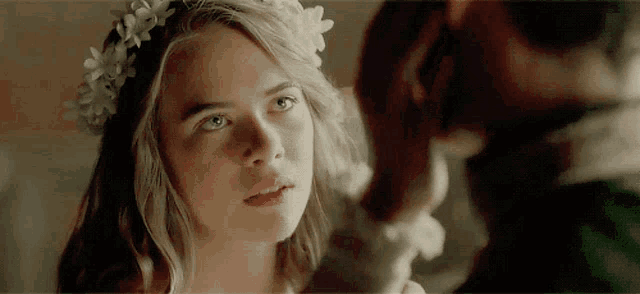 a young girl with a flower crown on her head looks at a man .