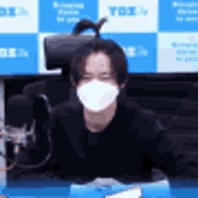a man wearing a mask is sitting at a desk in front of a microphone .