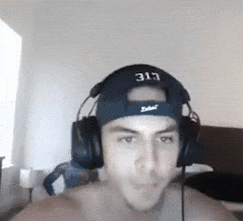 a man wearing headphones and a baseball cap is sitting on a bed .