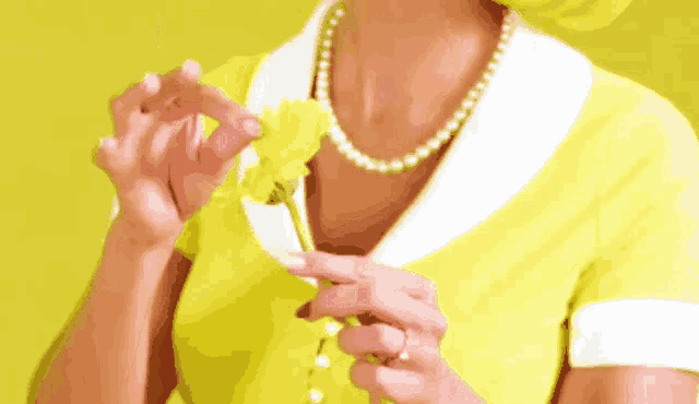 a woman in a yellow dress is holding a yellow flower .