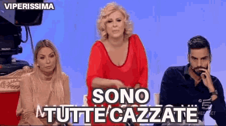 a woman in a red top is standing next to a man and a woman with sono tutte cazzate written on the bottom