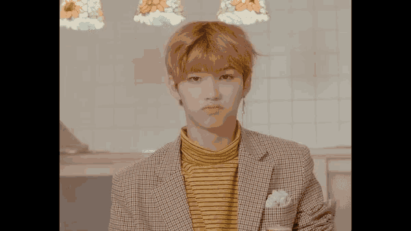 a young man wearing a plaid jacket and a yellow striped shirt looks at the camera