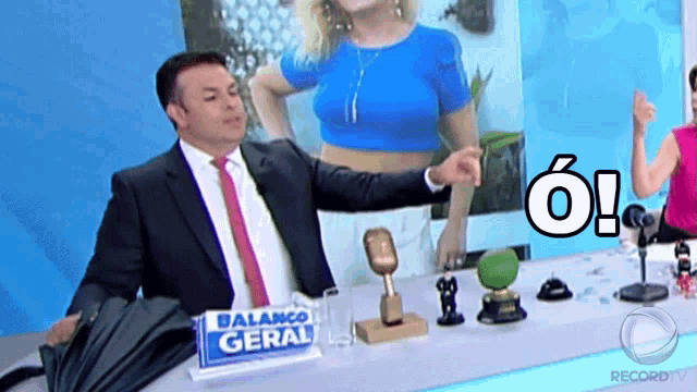 a man in a suit and tie is sitting at a table with a sign that says balanco geral