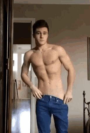 a shirtless man in blue jeans is standing in a room with his hands in his pockets .