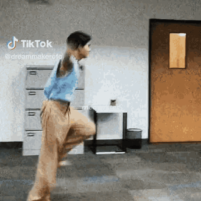 a woman in a blue shirt and khaki pants is jumping in the air in a room .