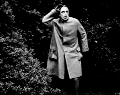 a black and white photo of a man in a coat standing in the woods